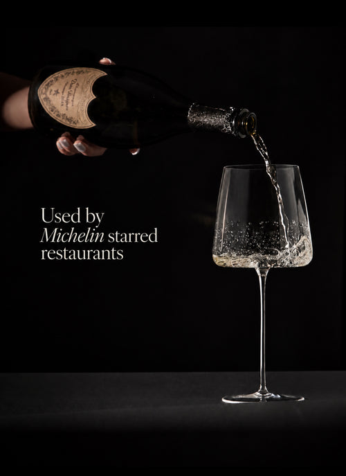 A hand holds a dark wine bottle pouring clear liquid into a stemmed wine glass against a black background, with white text reading 'Used by Michelin starred restaurants'.